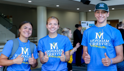 three students smilling for the camera with thumbs ups